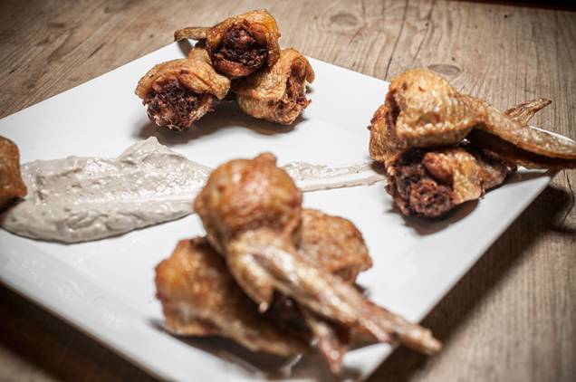 Crocantes, as asinhas de frango recheadas de carne-seca vêm no prato manchado por creme de azeitonas Crocantes, as asinhas de frango recheadas de carne-seca vêm no prato manchado por creme de azeitonas