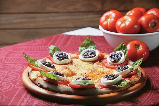 Caprese: cobertura de mussarela e fatias de tomate coroadas por uma composição de mussarela de búfala, folhas de manjericão gigante e pesto de azeitona preta Caprese: cobertura de mussarela e fatias de tomate coroadas por uma composição de mussarela de búfala, folhas de manjericão gigante e pesto de azeitona preta