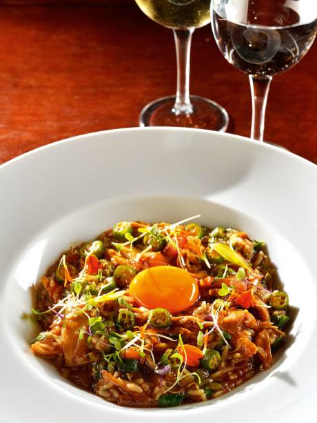 Os grãos úmidos misturados a galinha e a quiabo são coroados por uma gema curada e brotos Os grãos úmidos misturados a galinha e a quiabo são coroados por uma gema curada e brotos