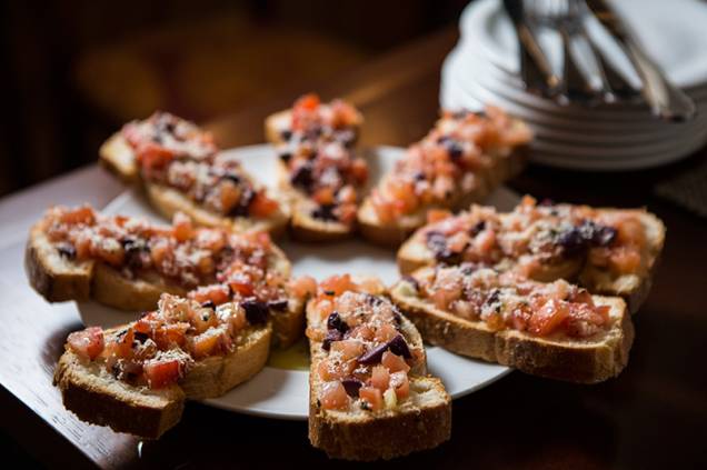 Montadas sobre um pão macio, a porção de enormes bruschettas traz tomate picado, azeitona preta e parmesão Montadas sobre um pão macio, a porção de enormes bruschettas traz tomate picado, azeitona preta e parmesão