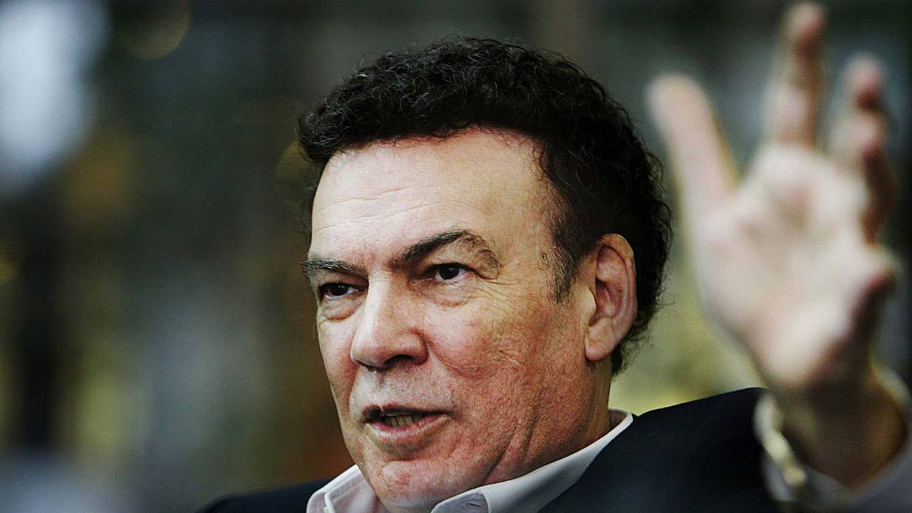 Retrato de homem branco com cabelos pretos vestindo camisa e suéter preto por cima