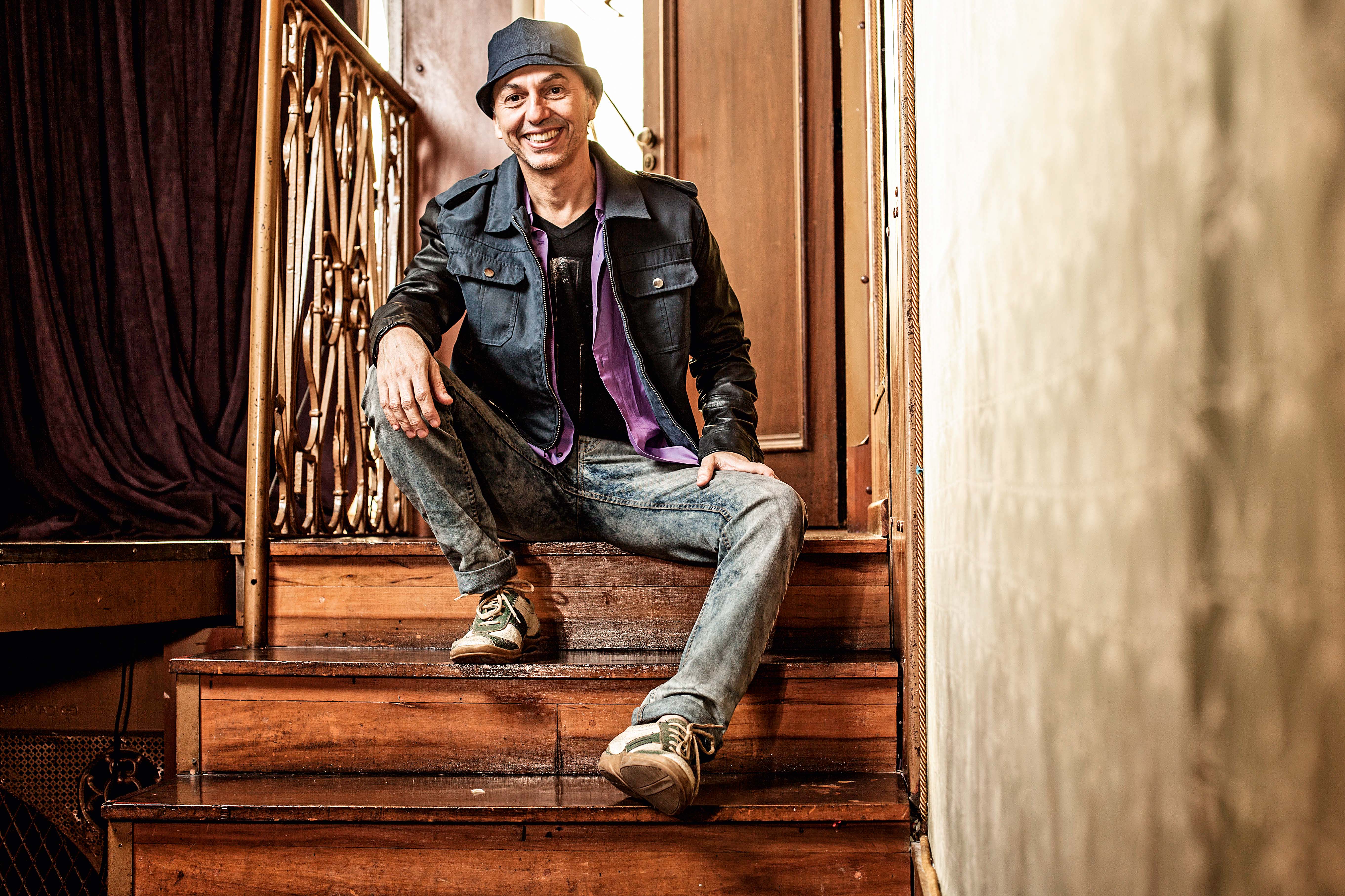 Zeca Baleiro posa sentado em escada de madeira.