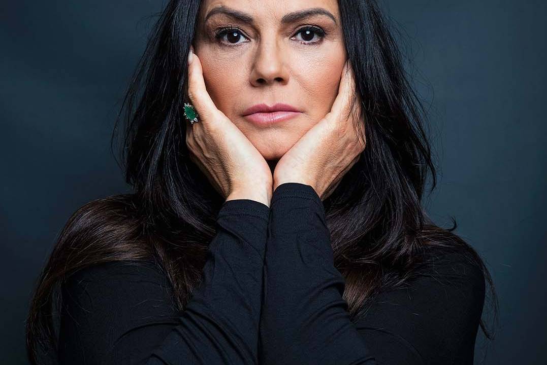 Luiza Brunet posa para a camera; ela está com as mãos no rosto