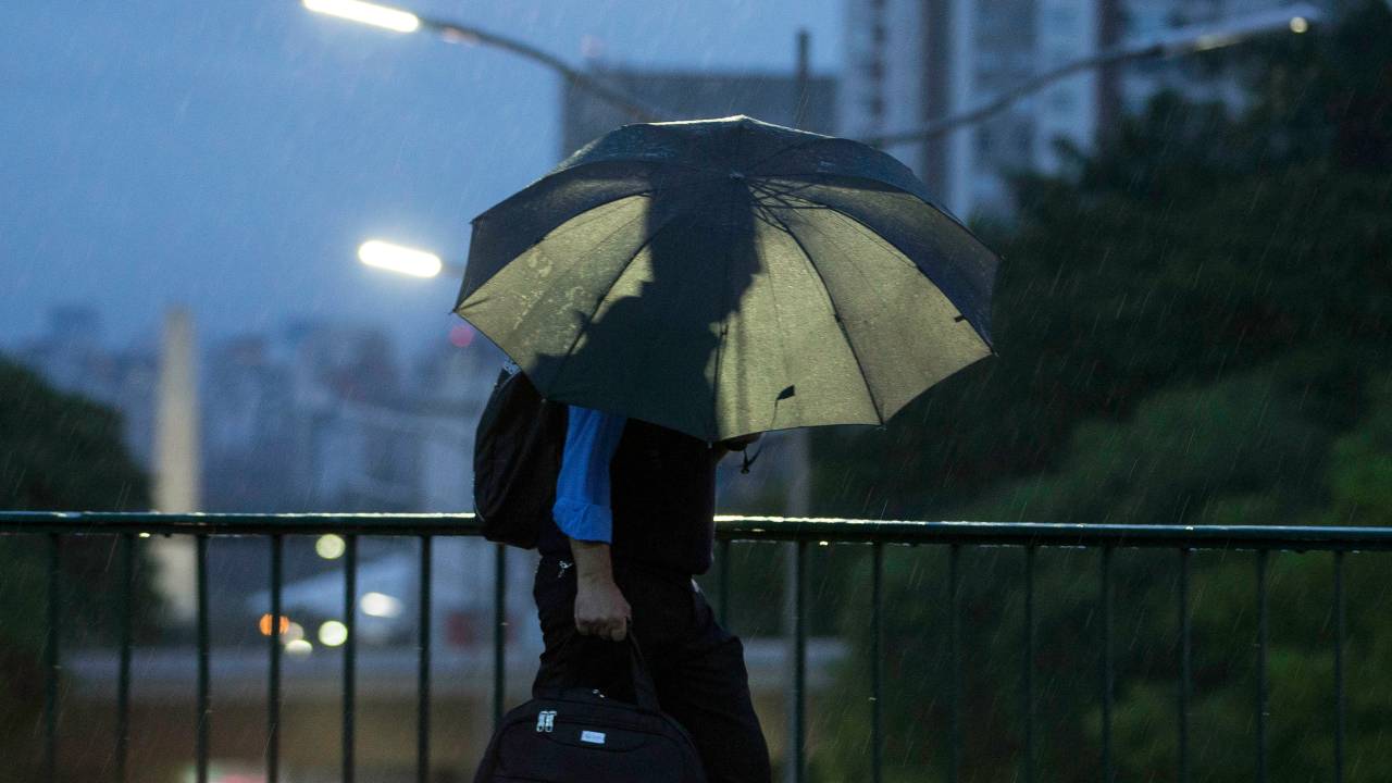 Imagem mostra pedestre caminhando com guarda-chuva