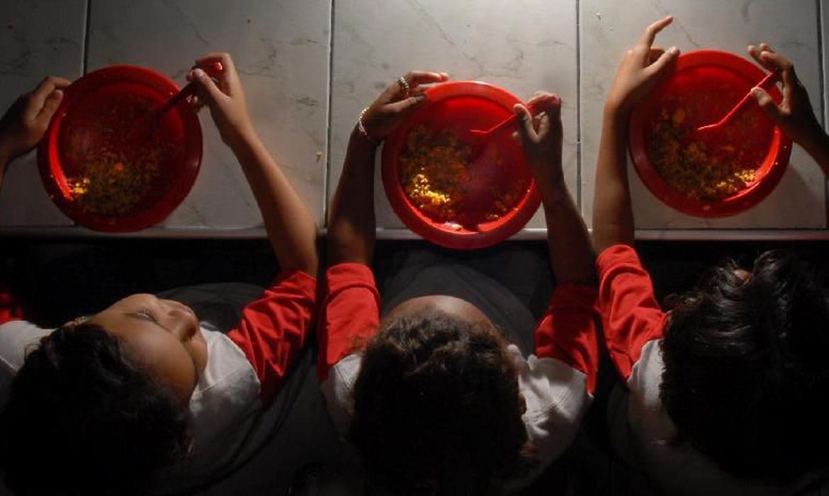 Crianças sentadas comem merenda escolar