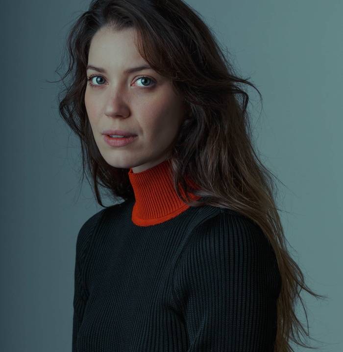 Nathalia Dill encara a câmera e veste suéter preto com gola vermelha.