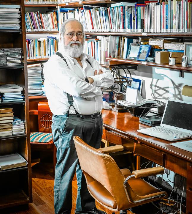 Gonzalo Vecina Neto, de pé e braços cruzados, em um escritório olhando para câmera com cara séria