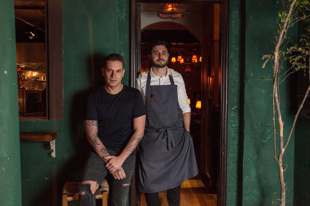 Os chefs Rodolfo De Santis e Julian Rigo Dois homens, um de camiseta preta e um de avental, posam em restaurante