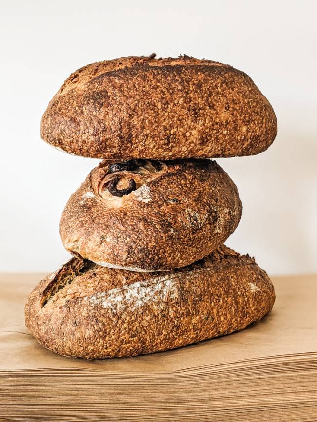 quatro pessoas agachadas com o rosto coberto por máscaras protetoras segurando canecas dentro de uma cozinha