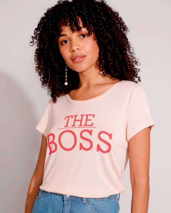 Mulher negra com cabelos cacheados veste blusa rosa com o escrito 