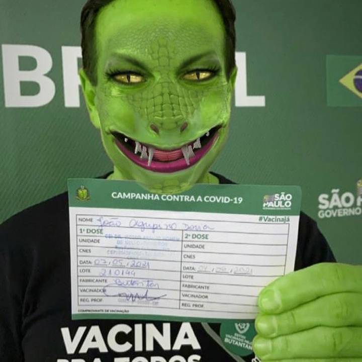 Imagem de Doria segurando o certificado de vacinação. Um filtro o faz ficar parecido com um jacaré