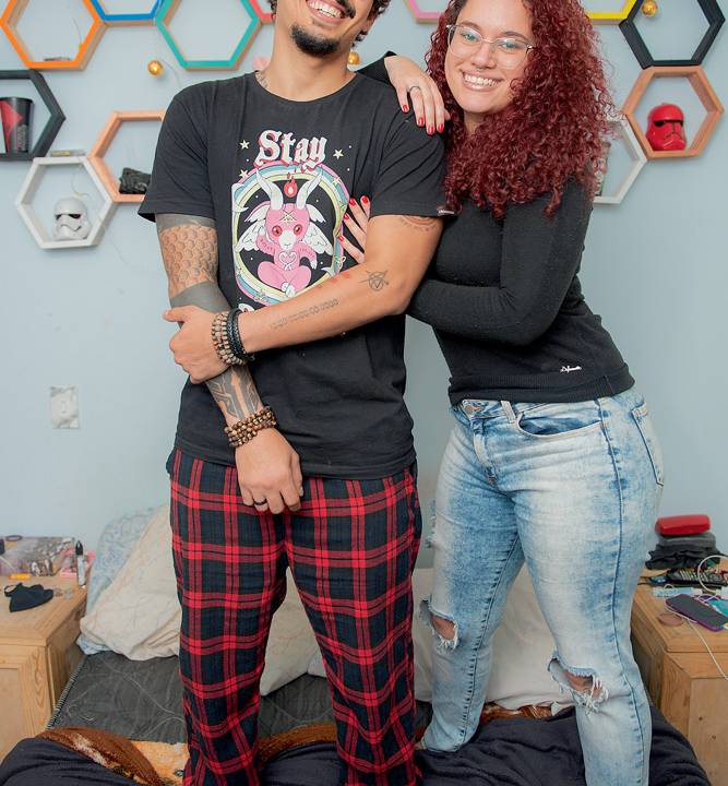 Rodrigo e Juliana em pé, em cima da cama, posando para a foto. Ele está com o braço sendo seguro por uma das mãos e Juliana se apoia nele pelo ombro