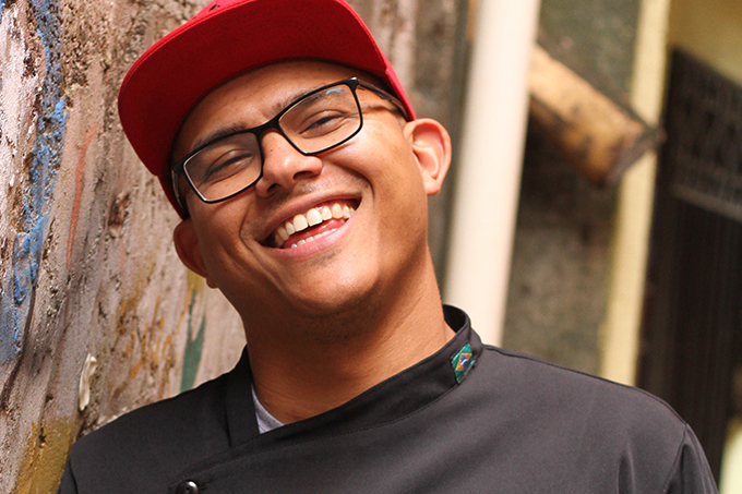 Edson Leite, apoiado em parede à esquerda, usando boné e óculos de grau aparece sorrindo para a foto. Vestido com dólmã cinza com seu nome.