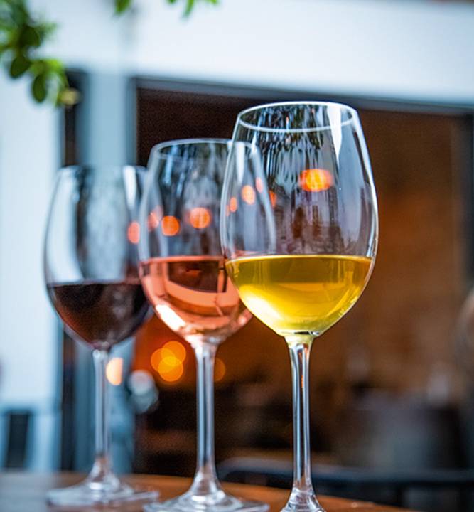 Na imagem aparece três taças de vinhos. Uma com tinto, outra com rosé a ultima com vinho branco.
