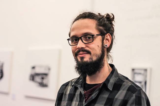 artista.jpg Homem de óculos e cabelo em um coque posa para foto