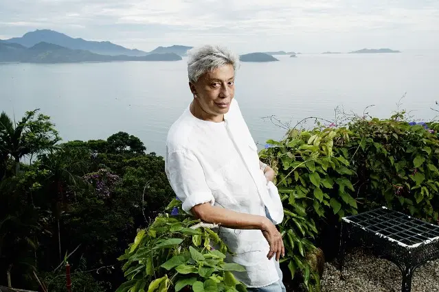 Homem posa de branco em cima de uma casa que tem vista para o oceano