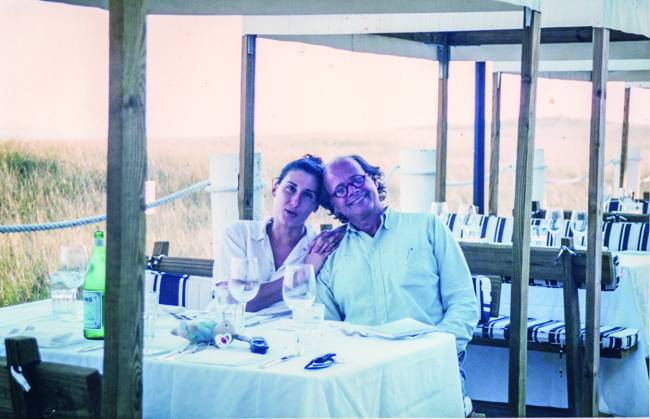Paola Carosella Mulher (à direita) e homem sentados abraçados em mesa de restaurante.