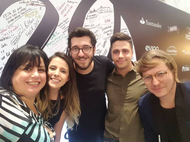 Cinco pessoas (duas mulheres no canto esquerdo e três homens à direita) reunidas em frente ao painel de 20 anos de Comer & Beber.