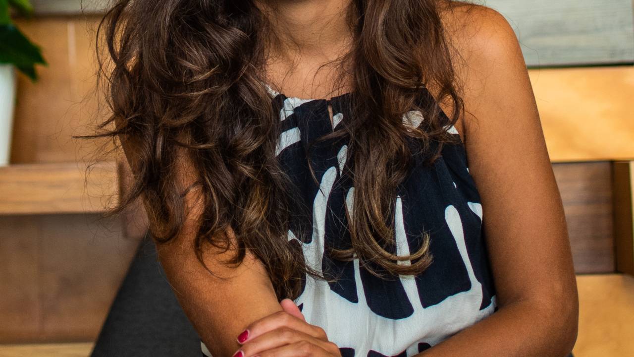 Aryanne Valgas sorri para a câmera sentada, vestindo peça em preto e branco.