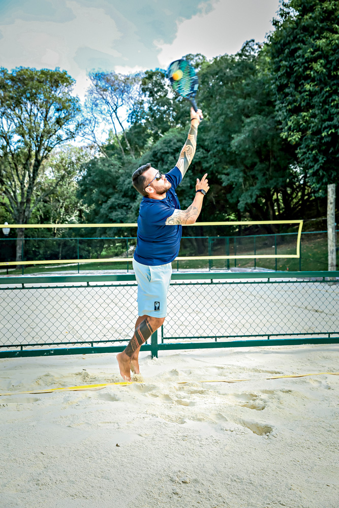 DANIEL_SAQUE_1.JPG A imagem mostra o professor acertando a bola de beach tennis em uma quadra de areia.