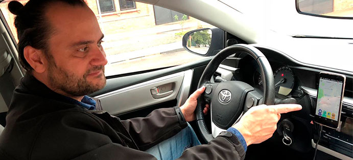 Imagem de Marlon sentado no banco do motorista, dentro do carro, apontando para um celular