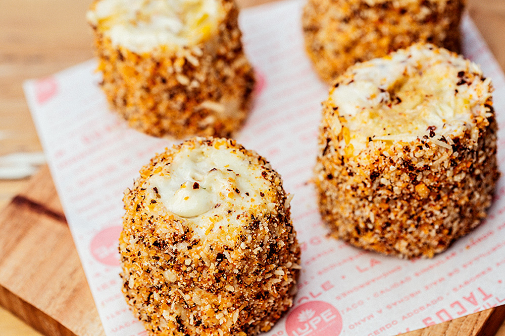 Pedaços de elotes sobre papel que leva o logo do luper bar y taquería.