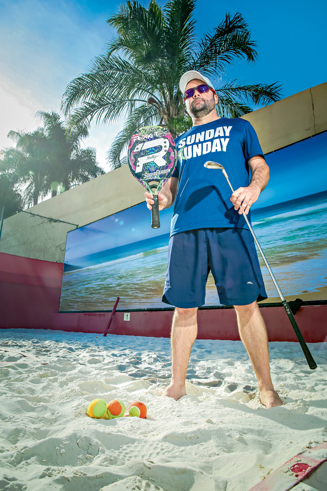PhilippeGasnier_1.JPG_1 A imagem mostra Philippe, em uma quadra de beach tennis, com sua raquete e taco de golf. Ele está com óculos escuros e boné.