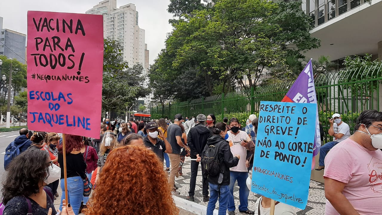 Funcionários da educação reunidos em frente à Câmara municipal pedindo vacina a professores. Uma placa diz "vacina para todos"