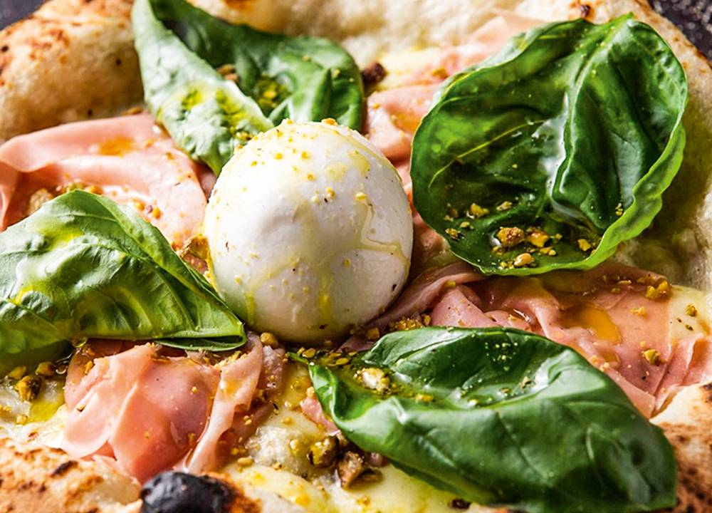 Pizza de presunto cru com folhas grandes de manjericão e burrata.