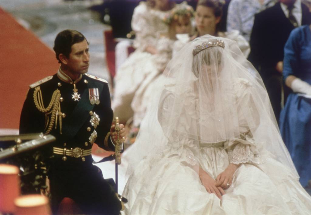 40-anos-casamento-principe-charles-princesa-diana-cerimonia-votos.jpg Príncipe Charles e sua esposa, a Princesa Diana, no altar da Catedral. charles segura uma espada apoiada em sua outra ponta no chão e diana está com o véu sobre sua face