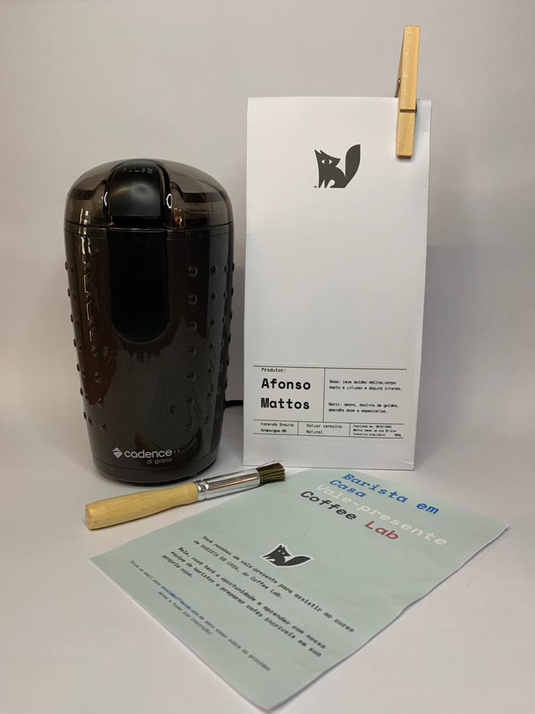 Kit com uma embalagem branca de caf&eacute; do lado direito, moedor de caf&eacute; e pincel e papel &agrave; frente.