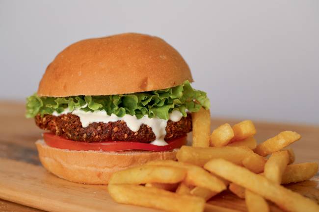 Hambúrguer de faláfel do Hamburguinho ao lado de fritas palito sobre mesa de madeira.