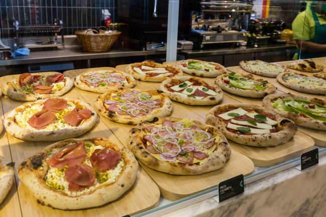 St Marche Pizzas individuais em vitrine sobre assadeiras de madeira.