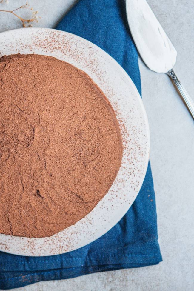 Foto aérea de bolo de chocolate em prata de louça branca sobre toalha azul.