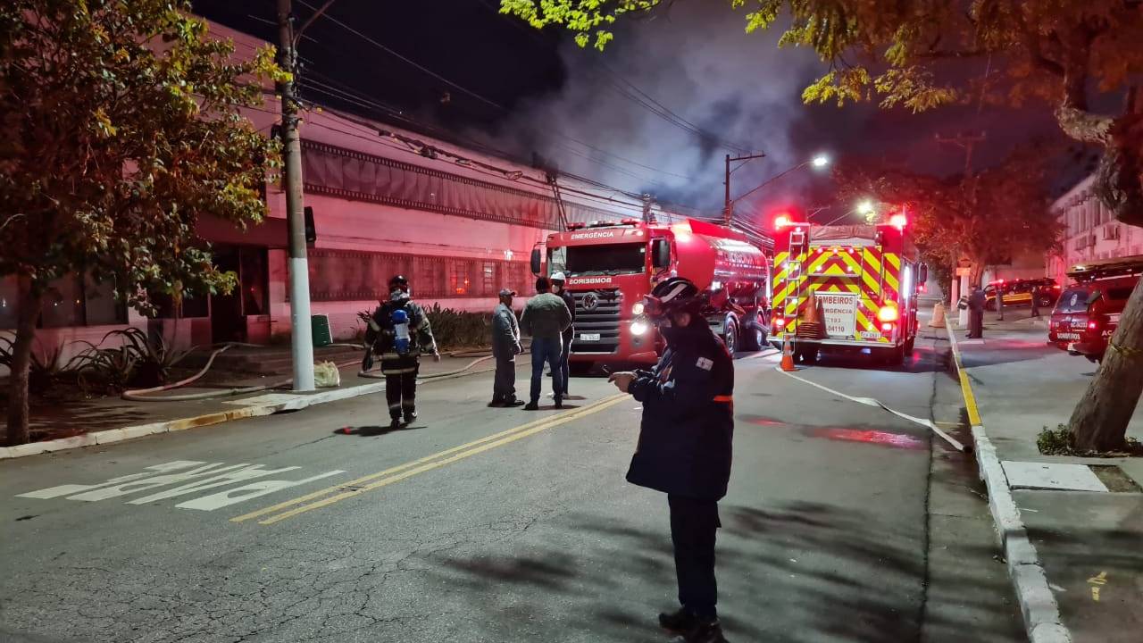 Imagem mostra rua com carros do corpo de bombeiros e edifício, de onde sai fumaça