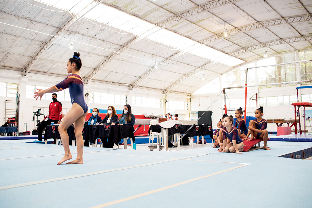 GINASTICA OLIMPICA INFANTIL A imagem mostra o centro de ginástica de São Bernardo. Crianças estão observado uma ginasta preparando para fazer um movimento
