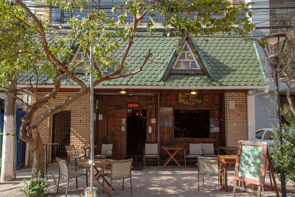 Achados ELO – Zur Alten Mühle Fachada do bar Zur Alten Mühle, com telhadinho verde e parede de tijolos.
