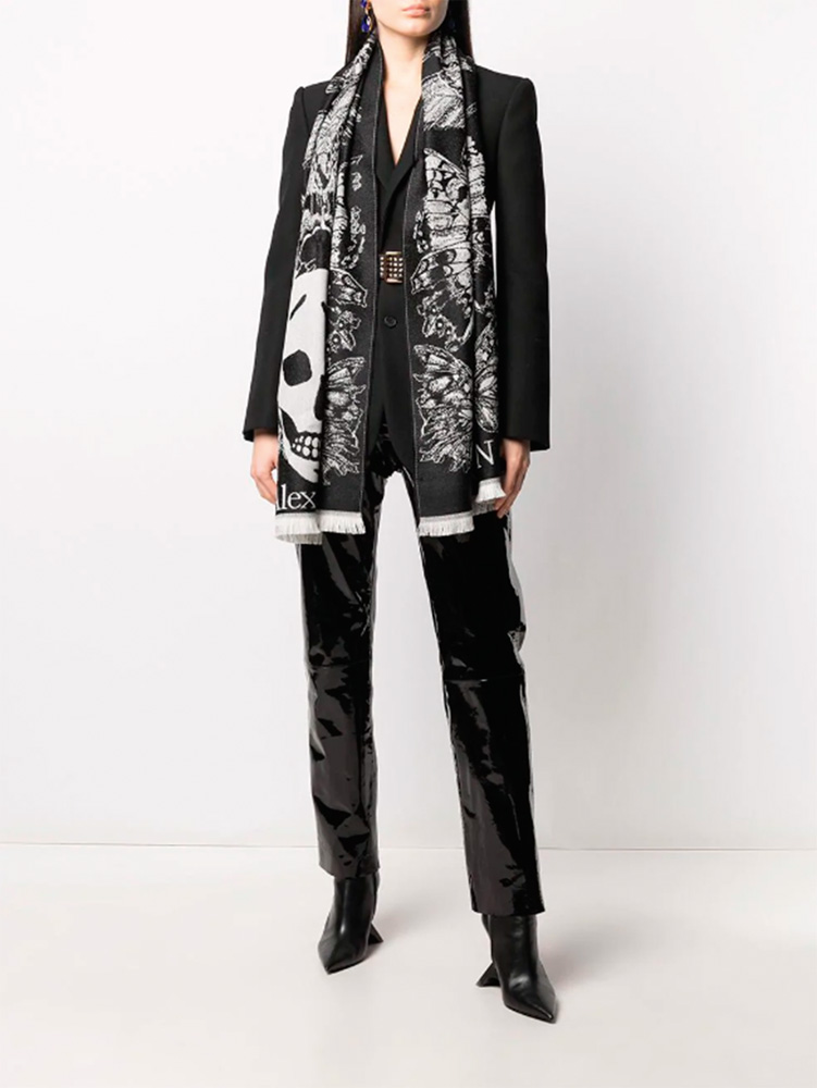 Imagem mostra s&oacute; corpo de mulher vestindo preto e um echarpe preto e branco com estampa de caveiras