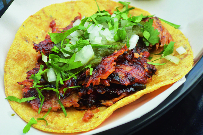 Tortilha de milho com recheio de carne e temperadas com folhas e cebola crua sobre folha de papel.