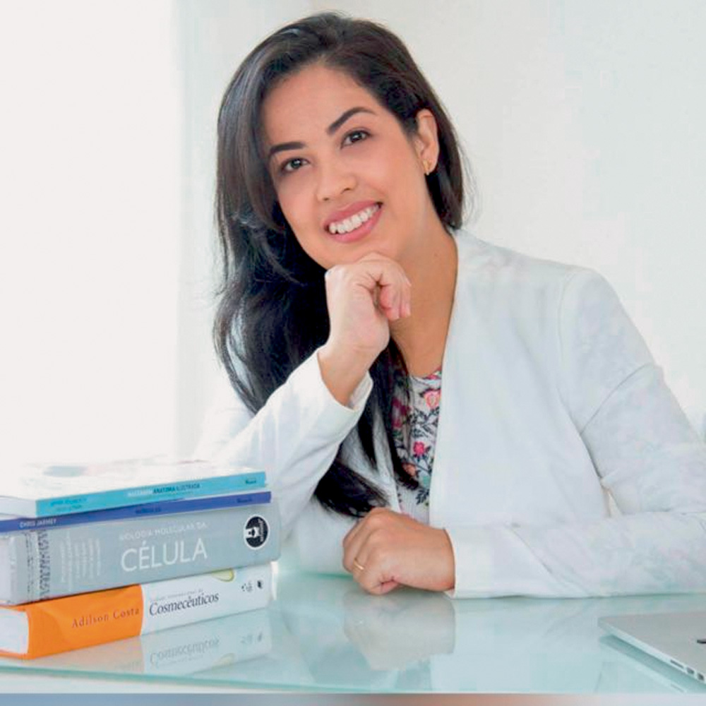 verdadeira-beleza-e-felicidade-visão-japonesa-lilian-sanpei-a-tal-felicidade lilian sanpei sentada com cotovelo direito apoiado na mesa e com cabeça sendo sustentada pela mão direita. ela está sorrindo para a foto