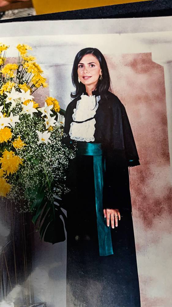 Ludhmila Hajjar formatura A imagem mostra Ludhmilla, com roupa de formatura, ao lado de flores.