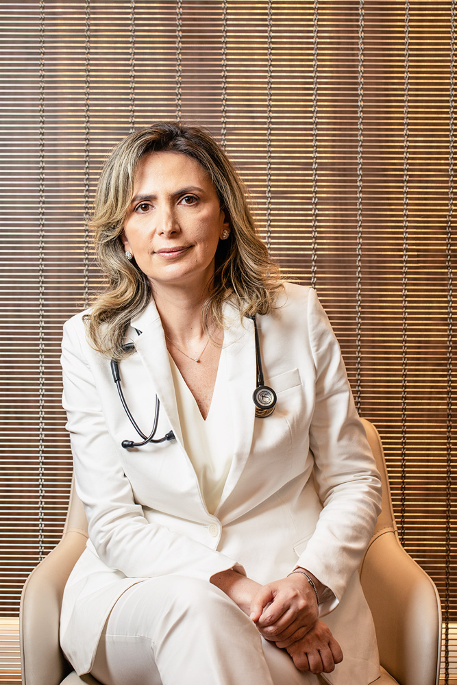 Ludhmila Hajjar Retrato da cardiologista Dra. Ludhmila Hajjar em seu consultório, na Vila Olímpia. Ela está de jaleco branco, com um estetoscópio nos ombros.