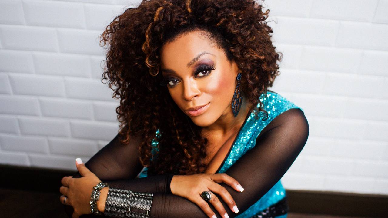 A cantora e compositora Paula Lima posa de braços cruzados com cabelo black-power e roupa na cor verde-água.