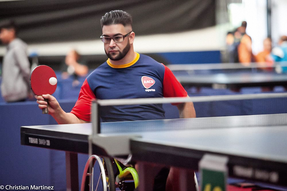 atletas-paralimpicos-amadores-experiências-pandemia-paralimpiadas-tóquio-paulo-oliveira.jpg foto de Paulo Oliveira jogando tênis. ele está sacando e na imagem aparece apenas uma parte da mesa e da rede