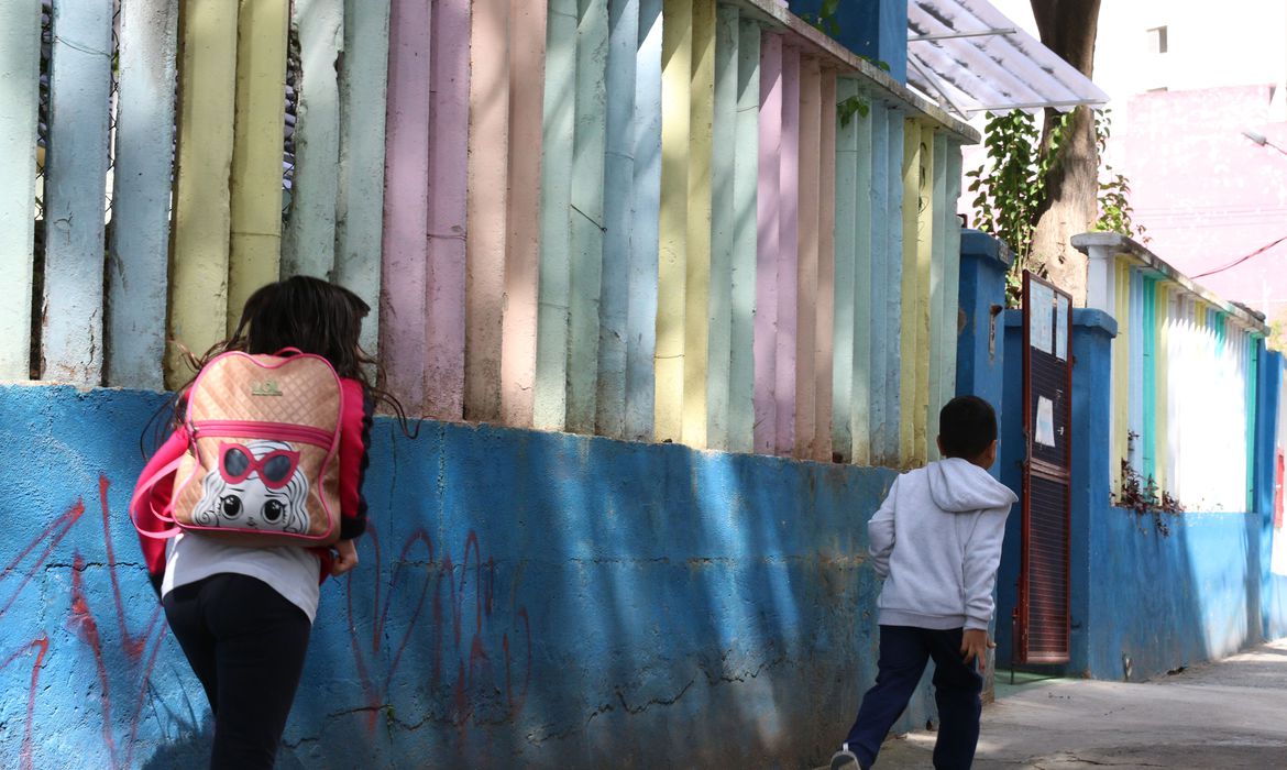 Imagem mostra alunos correndo na frente de escola