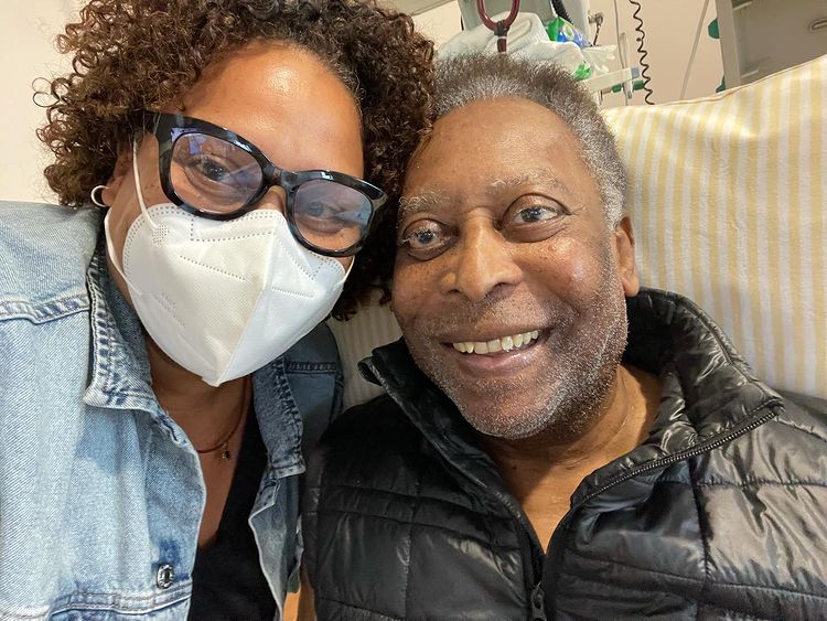 kely nascimento e pelé tirando selfie. ela está de máscara e óculos e ele está sentado em uma cama, com um colete preto, sem máscara e sorrindo