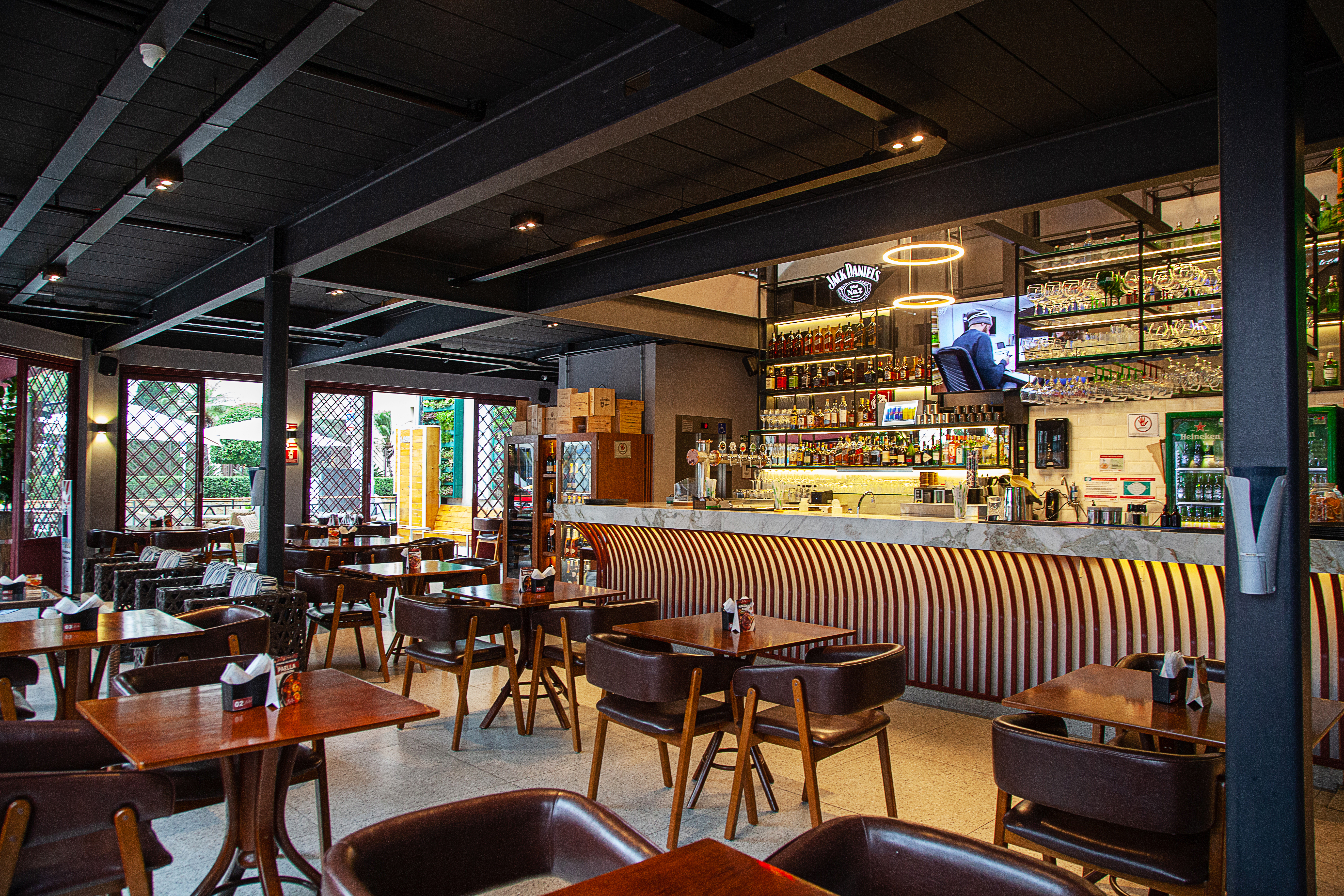 Sal&atilde;o do Martin Bar com balc&atilde;o e prateleiras de bebidas &agrave; direita e mesas de madeira com cadeiras forradas por couro espalhadas.