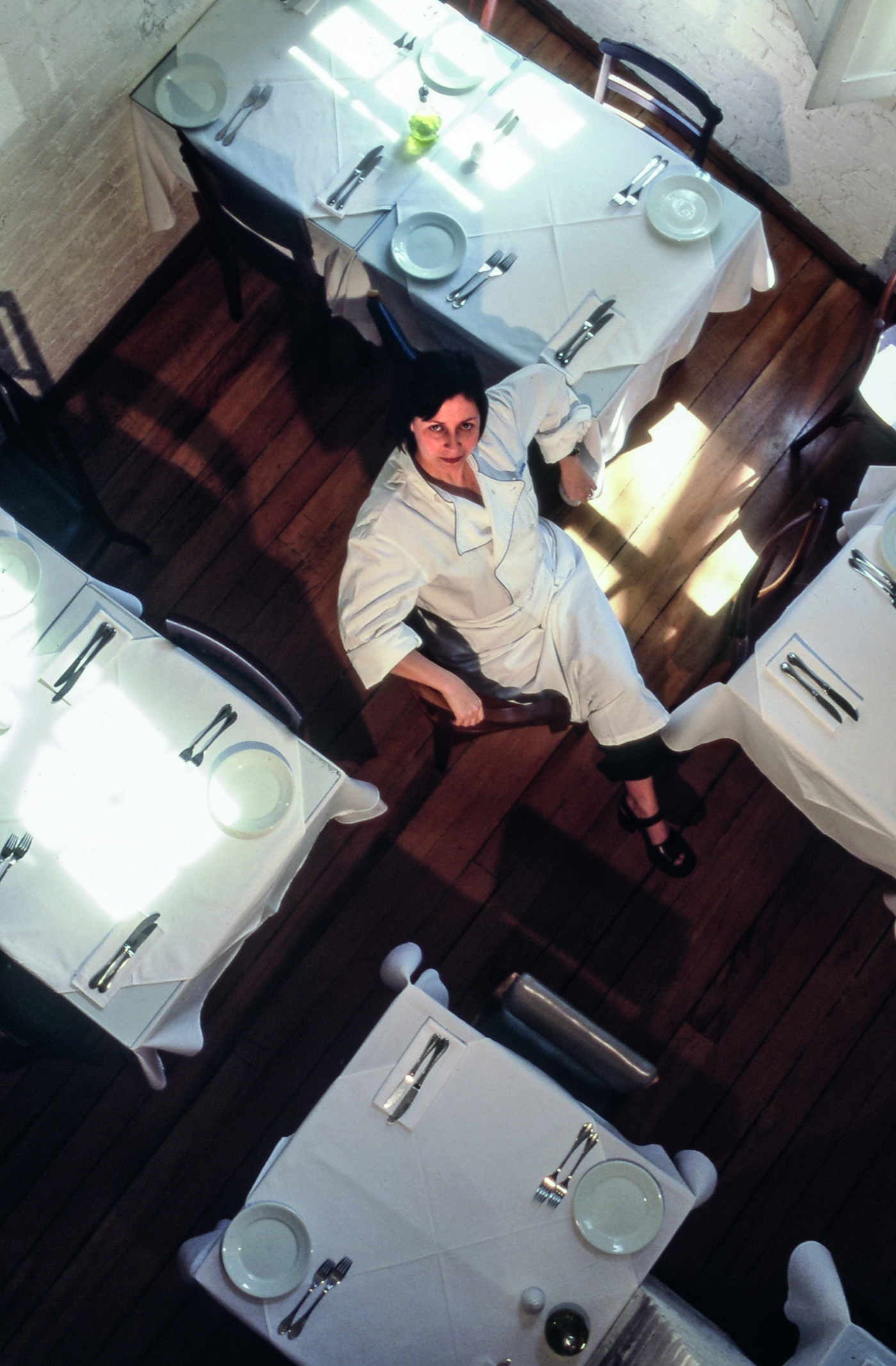 Foto a&eacute;rea da chef Carla Pernamuco sentada entre as mesas do sal&atilde;o do Carlota.