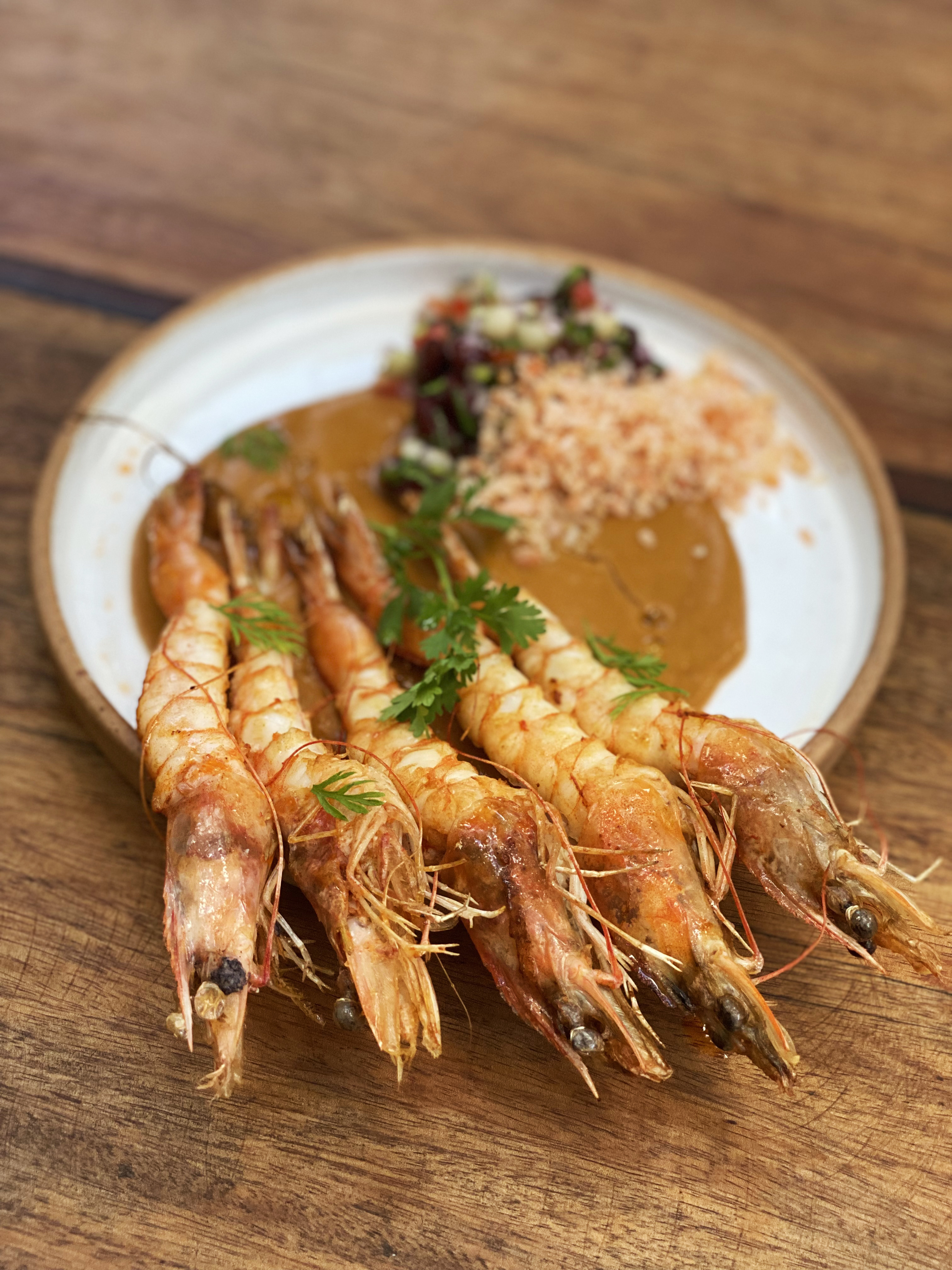 Prato de cer&acirc;mica com cinco camar&otilde;es grandes sobre molho terroso.