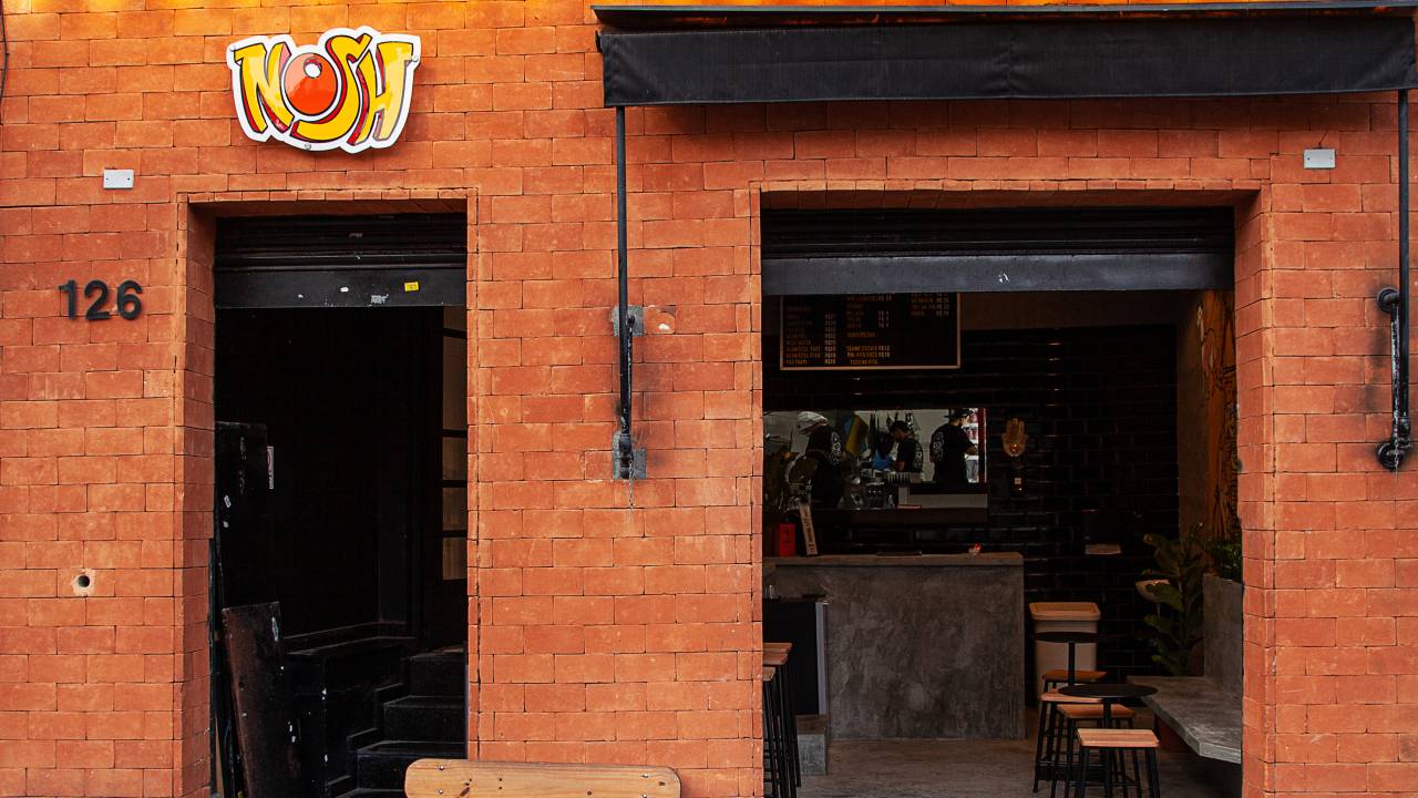 Fachada da lanchonete Nosh, com a parede laranja e banco de madeira na frente.